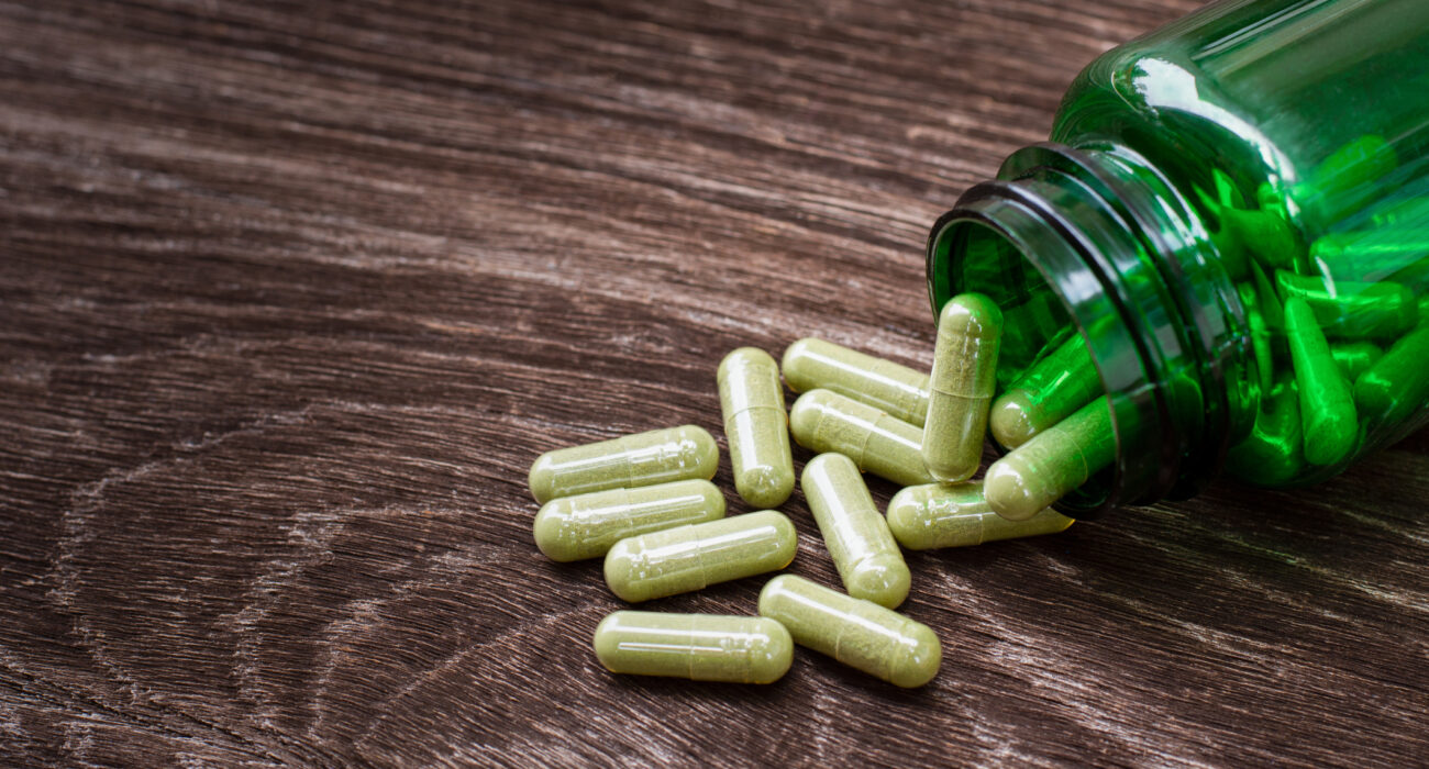 green bottle of kratom on table with pills spilling out