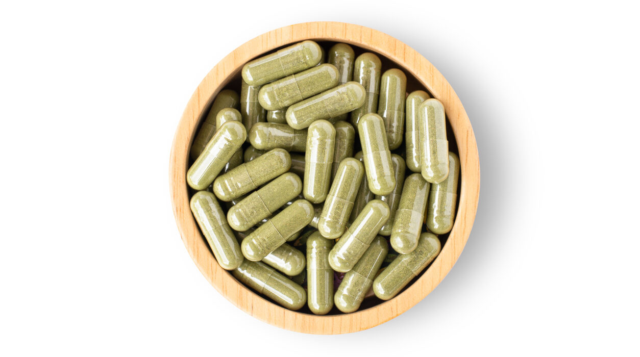 Green natural herbal medicine capsule pill in wooden bowl isolated on white background. Alternative supplement concept. Top view. Flat lay.