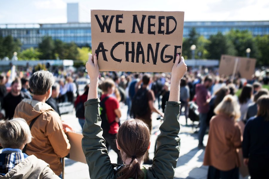 woman holds up sign at a rally saying "we need a change"